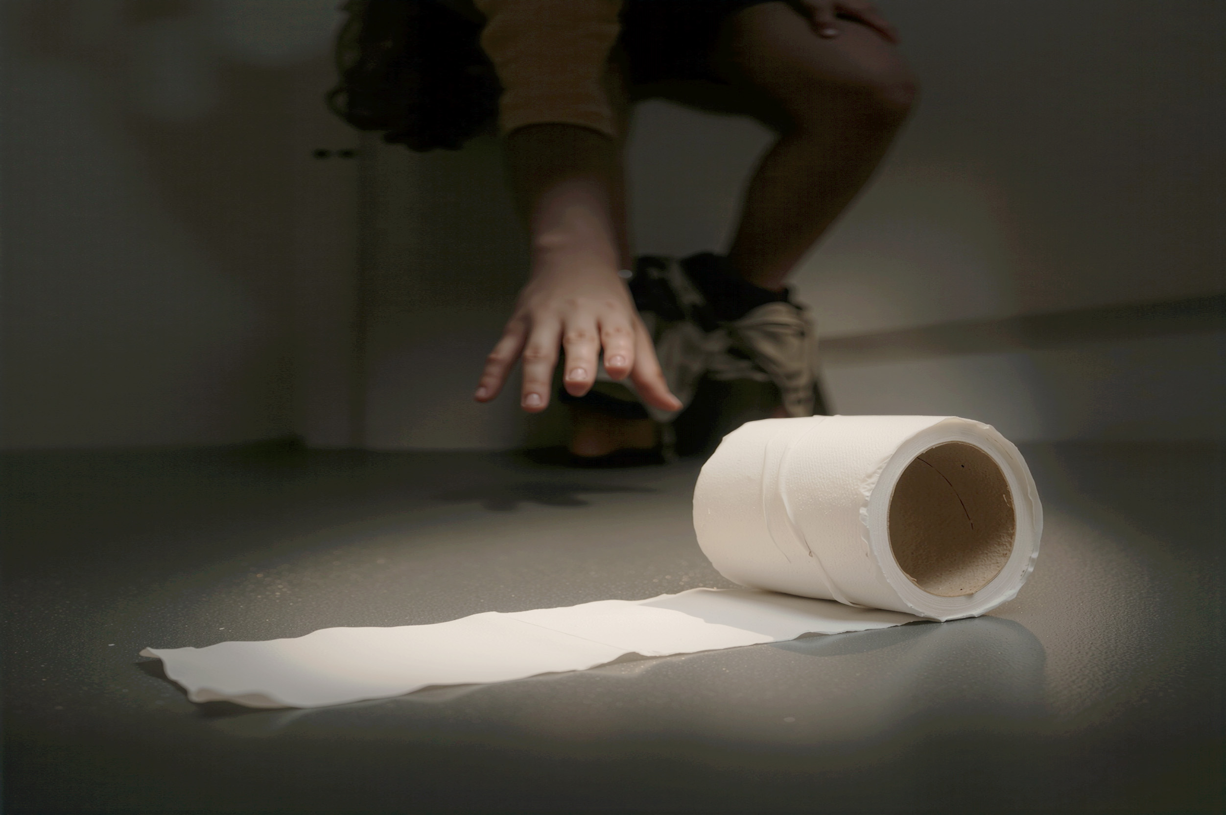 Person reaching for an unrolled toilet paper roll on the floor
